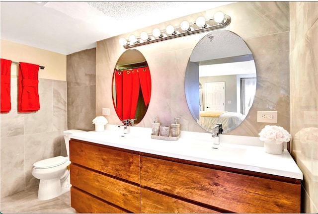 full bathroom featuring tile walls, toilet, double vanity, and a sink