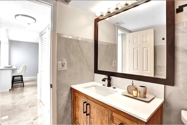 bathroom with visible vents, toilet, vanity, and tile walls