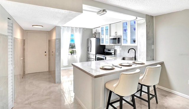 kitchen with a kitchen bar, a sink, appliances with stainless steel finishes, a peninsula, and light countertops