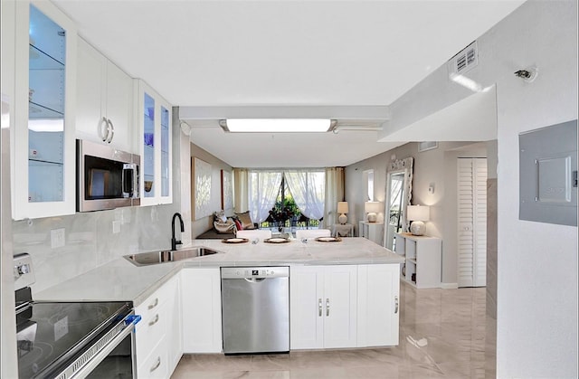 kitchen featuring glass insert cabinets, electric panel, a peninsula, stainless steel appliances, and a sink