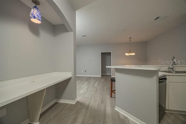 kitchen with a breakfast bar, sink, hanging light fixtures, light hardwood / wood-style floors, and kitchen peninsula