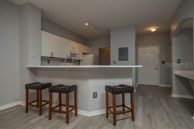 kitchen featuring white appliances, a breakfast bar, white cabinetry, light hardwood / wood-style floors, and kitchen peninsula