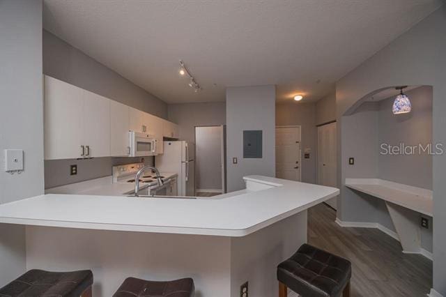 kitchen featuring a kitchen breakfast bar, electric panel, white appliances, and kitchen peninsula