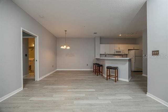 kitchen with pendant lighting, white appliances, light hardwood / wood-style flooring, white cabinetry, and kitchen peninsula