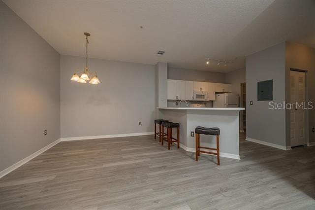 kitchen with white appliances, light hardwood / wood-style flooring, white cabinets, decorative light fixtures, and kitchen peninsula