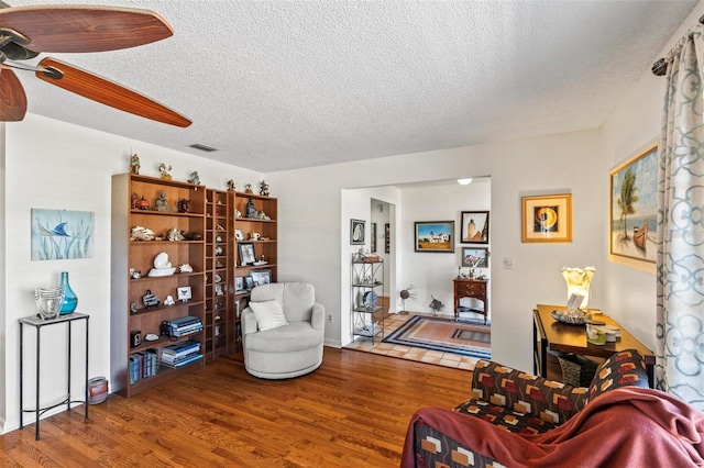 living area featuring hardwood / wood-style floors, ceiling fan, and a textured ceiling