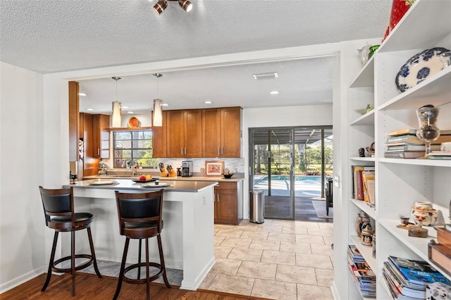 kitchen featuring kitchen peninsula, a breakfast bar, a textured ceiling, decorative backsplash, and pendant lighting