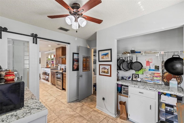 kitchen with double oven range, ceiling fan, a barn door, white cabinets, and light stone countertops