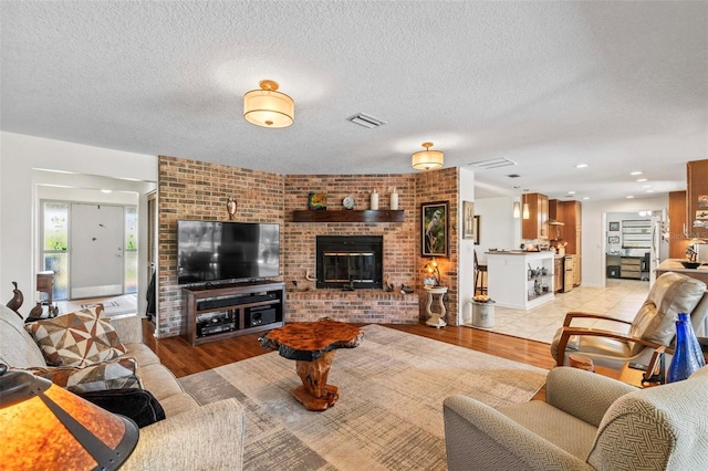 living room with a brick fireplace, light hardwood / wood-style floors, and a textured ceiling