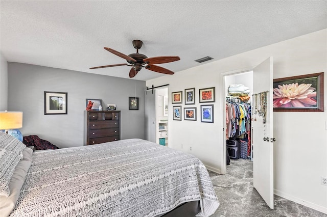 bedroom with light colored carpet, a walk in closet, a barn door, a closet, and a textured ceiling