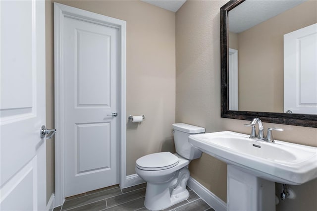 bathroom featuring toilet, baseboards, a sink, and wood finish floors