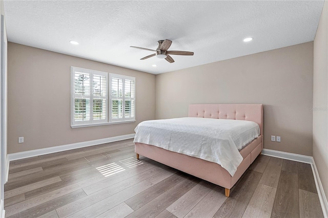 bedroom featuring ceiling fan, a textured ceiling, baseboards, and wood finished floors