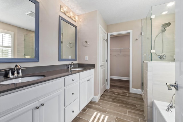 full bathroom with a stall shower, visible vents, a walk in closet, and a sink