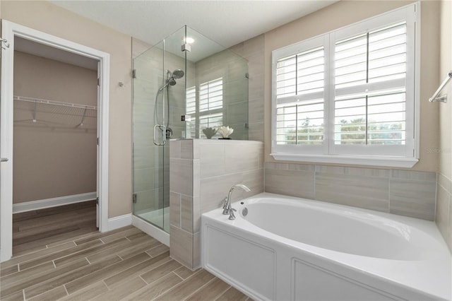 full bath featuring a walk in closet, wood finish floors, a stall shower, baseboards, and a bath