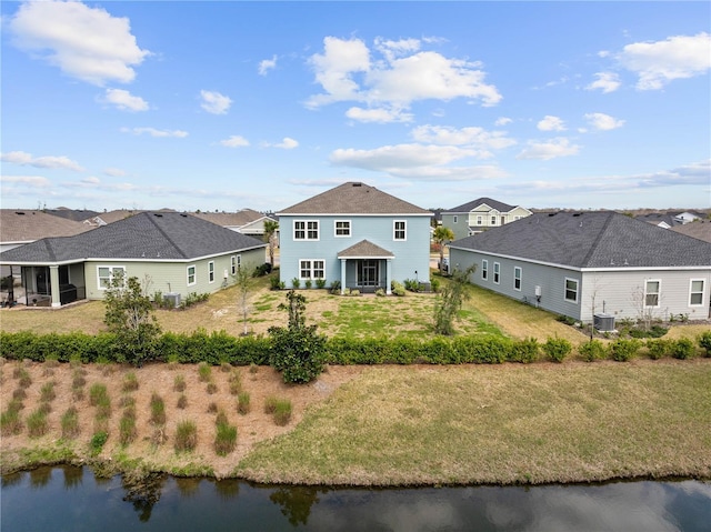 rear view of house with a residential view, a water view, a yard, and central AC