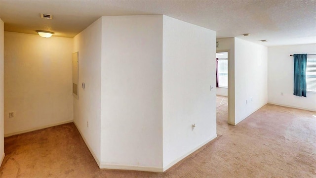 hallway with light colored carpet and a textured ceiling