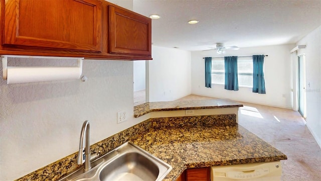 kitchen with sink, white dishwasher, kitchen peninsula, ceiling fan, and dark stone counters