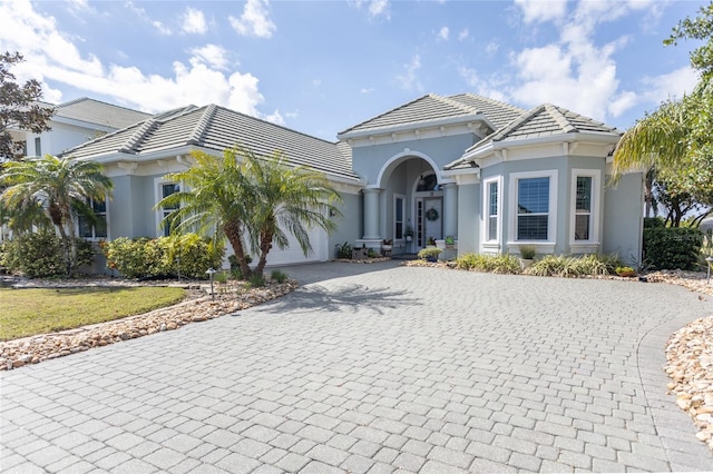 mediterranean / spanish-style house featuring an attached garage, a tile roof, decorative driveway, and stucco siding