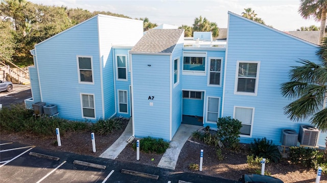 view of front of house with uncovered parking, a shingled roof, and central AC unit