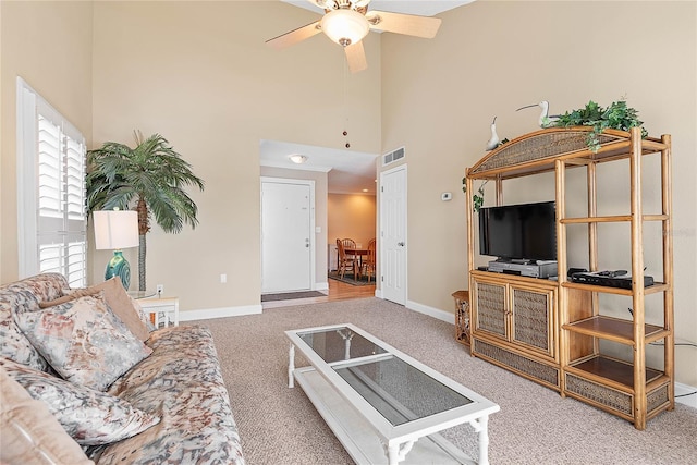 carpeted living area with visible vents, ceiling fan, a towering ceiling, and baseboards