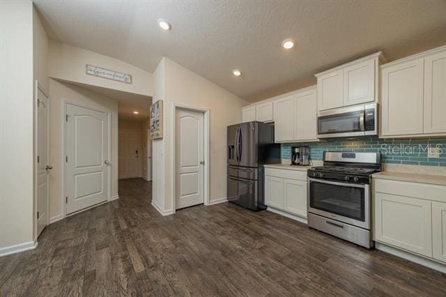 kitchen with vaulted ceiling, appliances with stainless steel finishes, dark hardwood / wood-style flooring, white cabinets, and backsplash