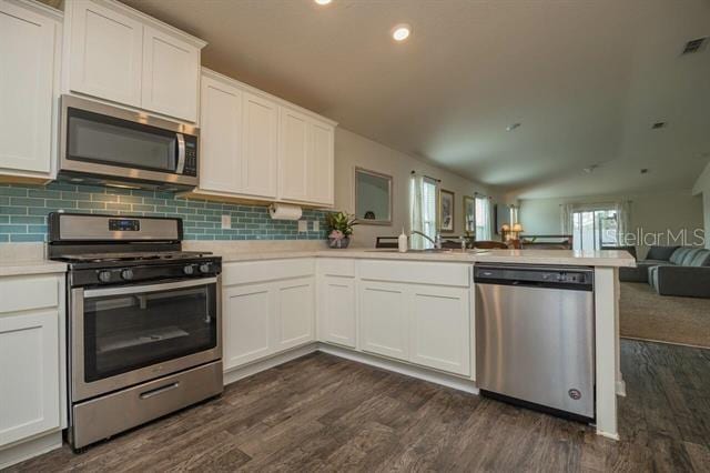 kitchen with appliances with stainless steel finishes, kitchen peninsula, sink, and white cabinets