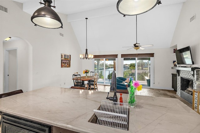 kitchen featuring ceiling fan, high vaulted ceiling, a fireplace, decorative light fixtures, and beamed ceiling