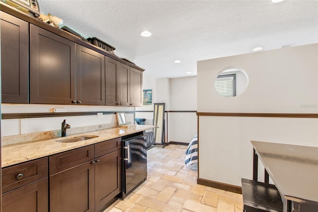 kitchen featuring black dishwasher, sink, light stone counters, dark brown cabinets, and a textured ceiling