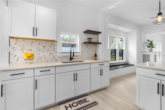 kitchen featuring decorative light fixtures, white cabinetry, sink, decorative backsplash, and light wood-type flooring
