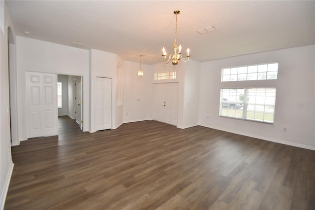 unfurnished room with dark wood-style floors, an inviting chandelier, visible vents, and a healthy amount of sunlight