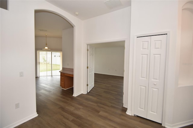 hall featuring arched walkways, dark wood-style floors, visible vents, and baseboards