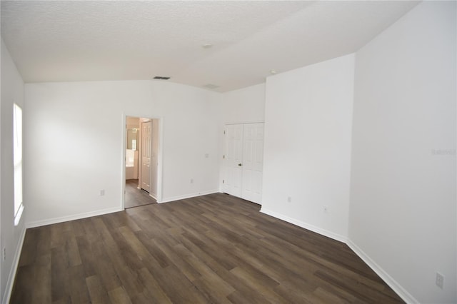 spare room featuring baseboards, visible vents, lofted ceiling, dark wood-style flooring, and a textured ceiling