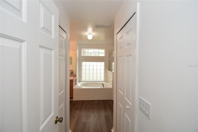 corridor with a textured ceiling, dark wood-type flooring, and visible vents