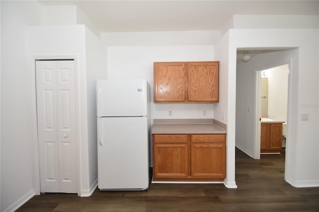 kitchen with baseboards, brown cabinetry, dark wood-style flooring, freestanding refrigerator, and light countertops