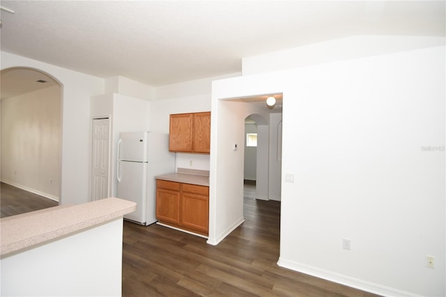 kitchen featuring brown cabinets, arched walkways, light countertops, and freestanding refrigerator