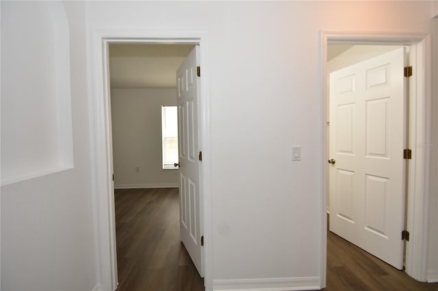 hallway featuring dark wood-type flooring and baseboards