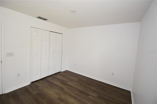 unfurnished bedroom featuring a closet, visible vents, dark wood-type flooring, a textured ceiling, and baseboards