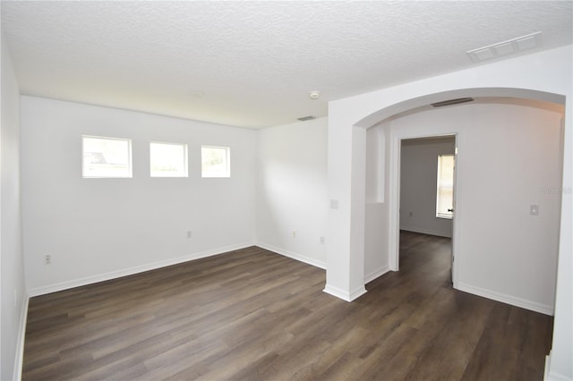 empty room featuring arched walkways, a textured ceiling, dark wood-type flooring, visible vents, and baseboards