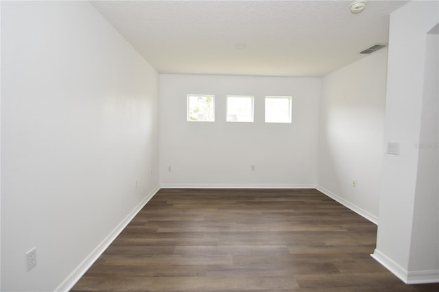 unfurnished room featuring dark wood-style flooring, visible vents, a textured ceiling, and baseboards