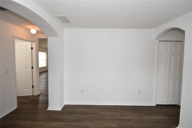 unfurnished room featuring arched walkways, visible vents, dark wood-type flooring, a textured ceiling, and baseboards