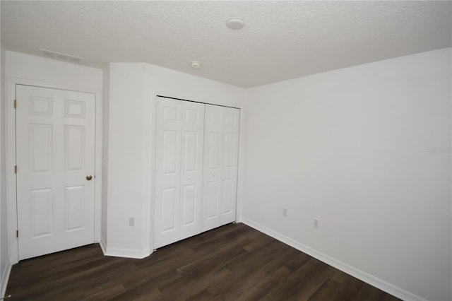 unfurnished bedroom featuring a textured ceiling, a closet, baseboards, and dark wood-style flooring