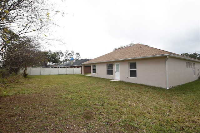 rear view of house with a lawn, fence, and stucco siding