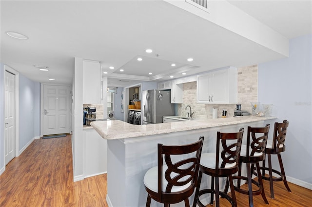 kitchen with stainless steel fridge with ice dispenser, sink, white cabinets, a kitchen breakfast bar, and kitchen peninsula