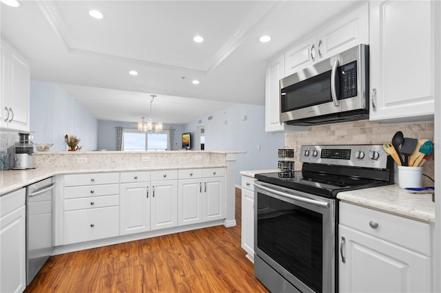 kitchen with appliances with stainless steel finishes, a tray ceiling, kitchen peninsula, and white cabinets