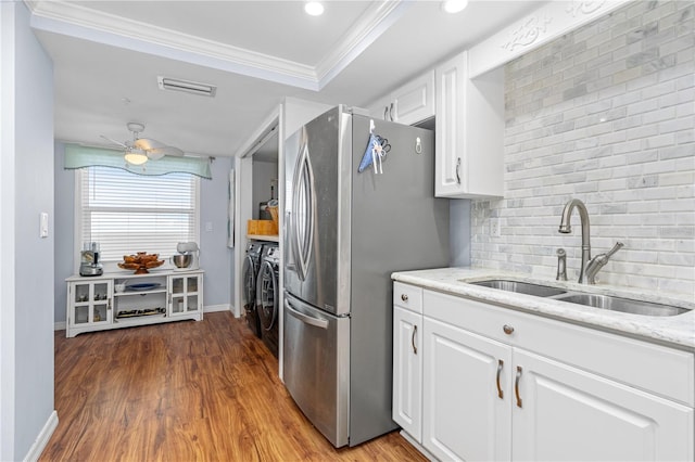 kitchen featuring sink, stainless steel fridge, white cabinets, crown molding, and washing machine and dryer