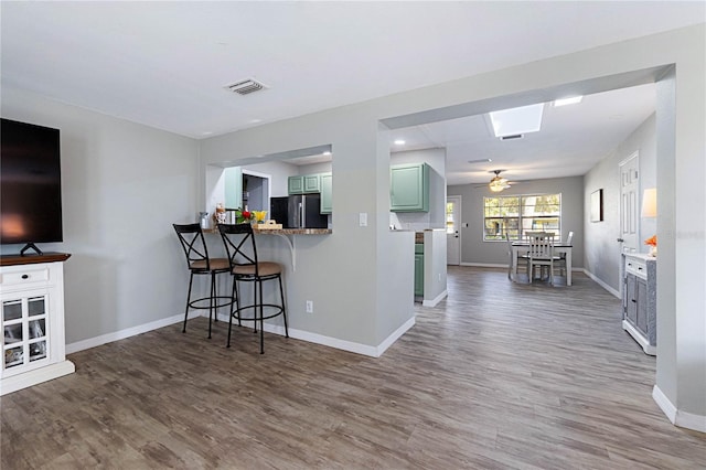 kitchen with a breakfast bar area, green cabinets, kitchen peninsula, black fridge, and dark wood-type flooring