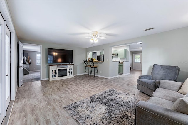 living room featuring ceiling fan, a wealth of natural light, a fireplace, and light hardwood / wood-style flooring