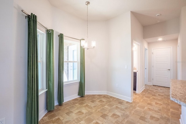 spare room with an inviting chandelier and baseboards