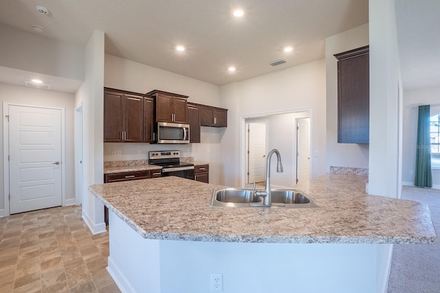 kitchen featuring light countertops, appliances with stainless steel finishes, a sink, dark brown cabinets, and a peninsula