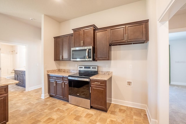 kitchen featuring light stone countertops, dark brown cabinetry, baseboards, and appliances with stainless steel finishes